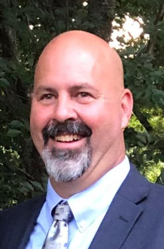 portrait of Brian Gearty wearing a suit, standing outdoors in front of a tree.